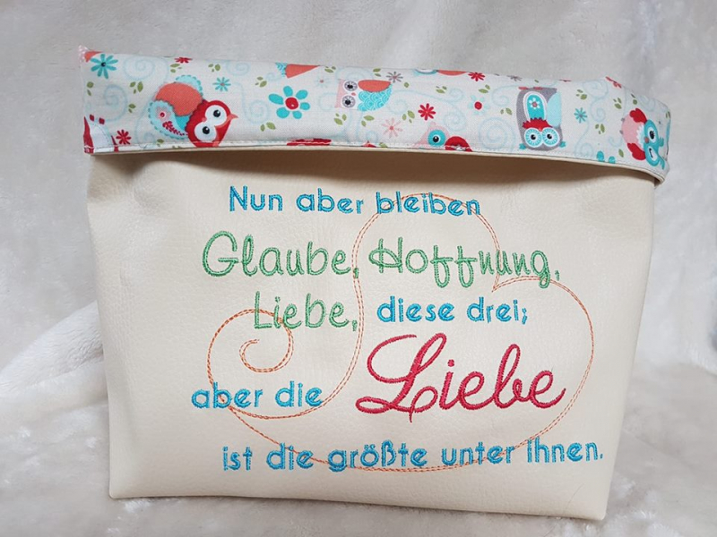 Stickdatei Set Glaube, Liebe, Hoffnung (div. Rahmengrößen), Foto zeigt helle Stofftasche mit umgeschlagenem Rand, der eulenbedrucktes Innenfutter erkennen lässt. Taschenbestickung Schnörkel-Herz, Schriftzug "Nun aber bleiben Glaube, Hoffnung, Liebe, diese